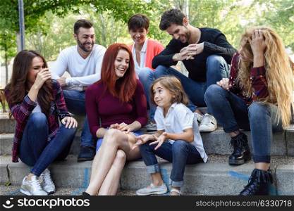 Young people together withe a little girl talking outdoors in urban background. Women and men sitting on stairs in the street wearing casual clothes.