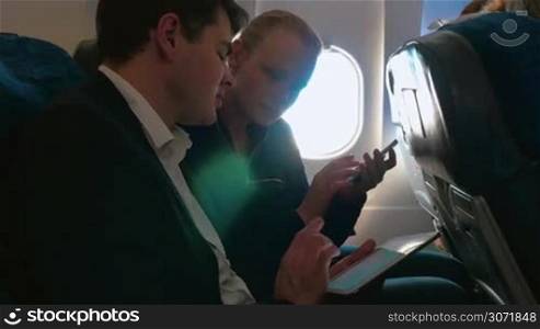 Young people traveling by plane and talking about business matters. Man explaining something to the woman using tablet computer