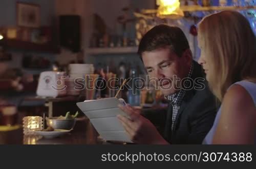 Young people using pad in the bar. Woman showing something tablet PC, man looking at screen and expressing agreement. Business in informal setting