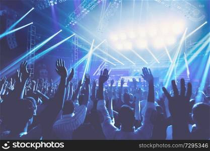 Young people with pleasure spending evening on the concert, crowd with raised up hands standing in blue lights, singing and enjoying music concept