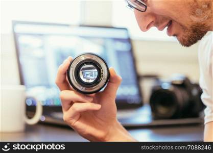 Young photographer is looking at a photography lens, laptop in the blurry background