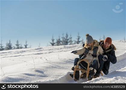 Young playful couple having fun in the snow sledging downhill
