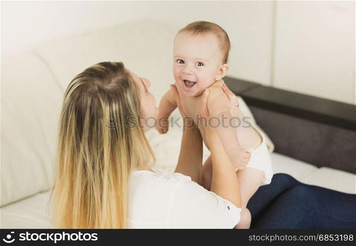 Young playful mother playing with her baby at bedroom