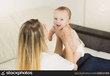 Young playful mother playing with her baby at bedroom