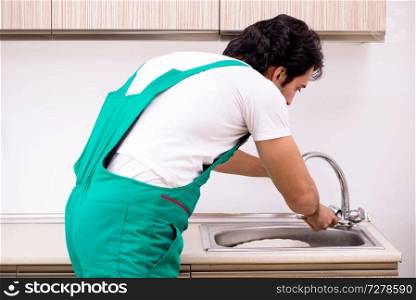 Young plumber repairing tap at kitchen  