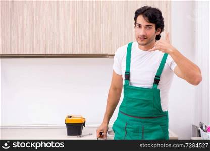 Young plumber repairing tap at kitchen  