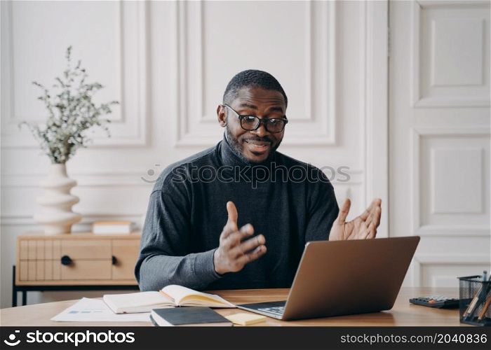 Young positive afro american man tutor talking with students during online lesson on laptop while working at home, happy african ethnicity guy speaking with colleagues via video call on computer. Young positive afro american man tutor talking with students during online lesson on laptop