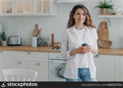 Young positive woman with phone in her stylish contemporary kitchen. Happy lady at home. Modern white scandinavian interior. Stove, worktop and cuisine.. Young positive woman with phone in her stylish contemporary kitchen. White scandinavian interior.