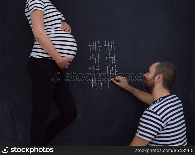 young pregnant couple accounts week of pregnancy and writing them with chalk on blackboard. pregnant couple accounts week of pregnancy