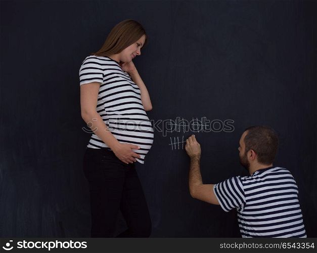 young pregnant couple accounts week of pregnancy and writing them with chalk on blackboard. pregnant couple accounts week of pregnancy