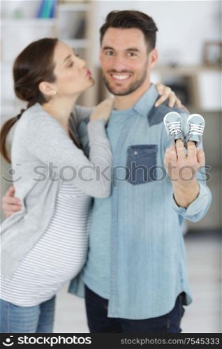young pregnant couple holding newborn baby shoes