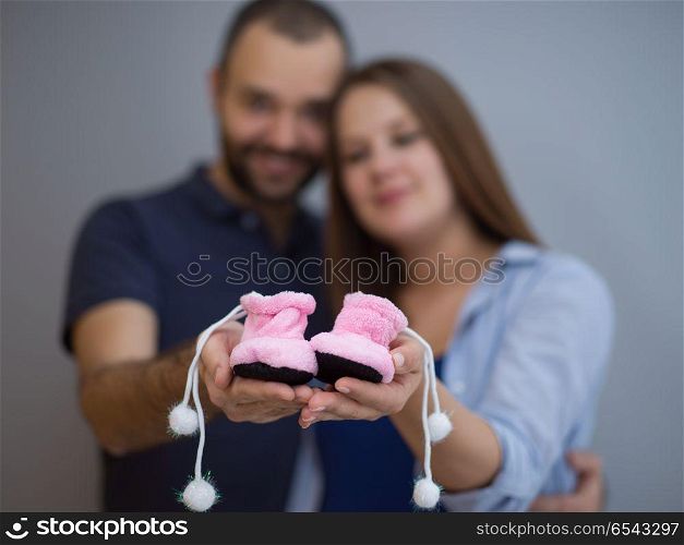 young pregnant couple holding newborn baby shoes isolated on white background in family and parenthood concept. pregnant couple holding newborn baby shoes