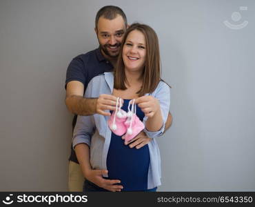 young pregnant couple holding newborn baby shoes isolated on white background in family and parenthood concept. pregnant couple holding newborn baby shoes