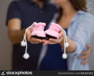 young pregnant couple holding newborn baby shoes isolated on white background in family and parenthood concept. pregnant couple holding newborn baby shoes