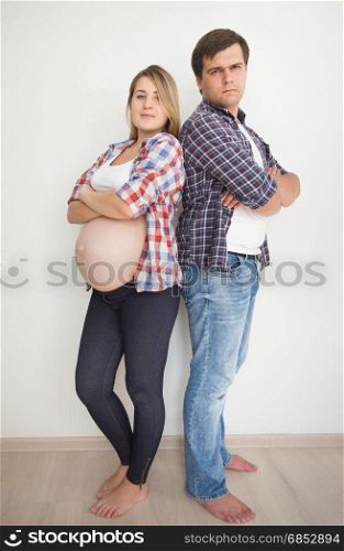 Young pregnant couple leaning on white wall at empty room