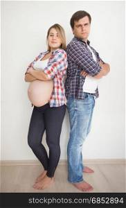 Young pregnant couple leaning on white wall at empty room
