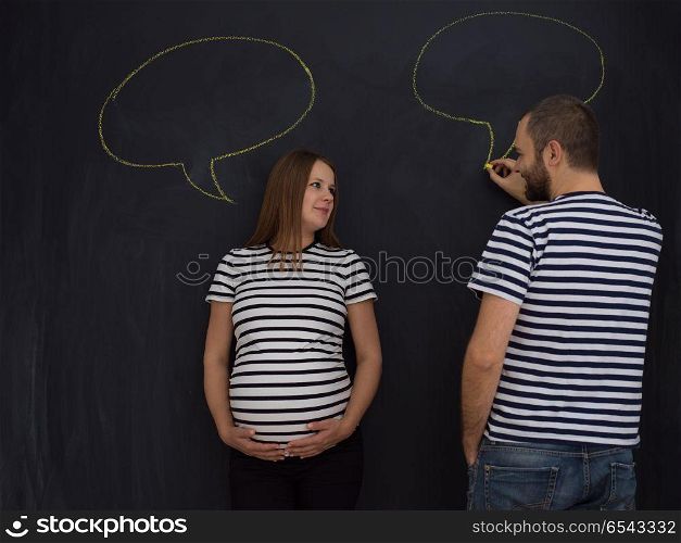young pregnant couple thinking about names for their unborn baby and writing them on a black chalkboard. pregnant couple writing on a black chalkboard