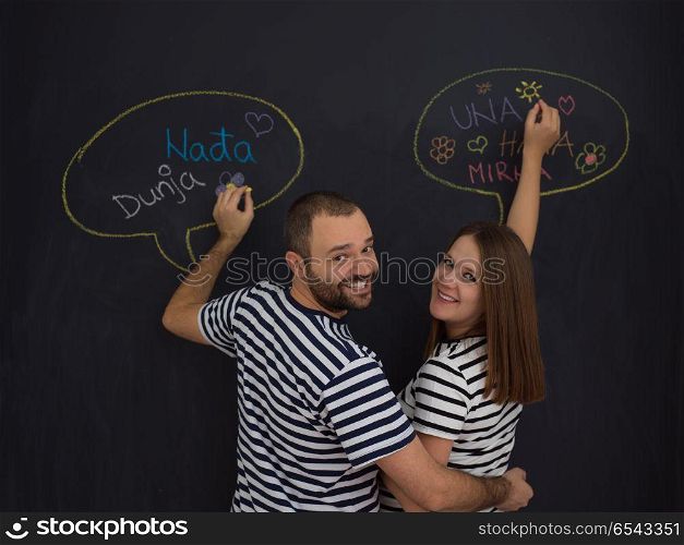 young pregnant couple thinking about names for their unborn baby and writing them on a black chalkboard. pregnant couple writing on a black chalkboard