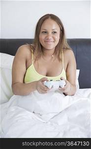 Young pregnant playing video game with remote control in bed