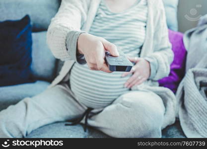 Young pregnant woman boring and watching tv at home