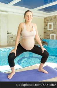 Young pregnant woman exercising in gym on fitness mat