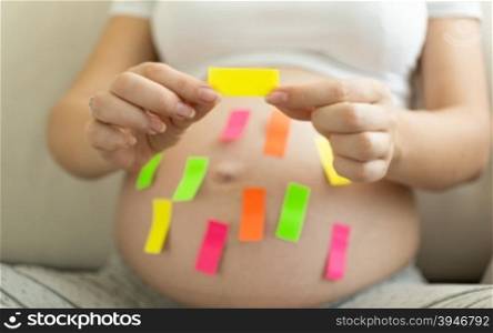 Young pregnant woman holding colorful memo stickers