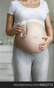 Young pregnant woman holding glass of water