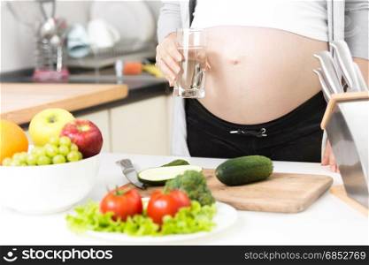 Young pregnant woman holding glass of water on kitchen