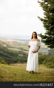 Young pregnant woman in white dress at the forest on a summer day