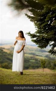 Young pregnant woman in white dress at the forest on a summer day