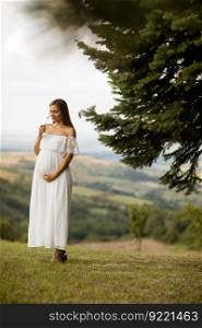 Young pregnant woman in white dress at the forest on a summer day
