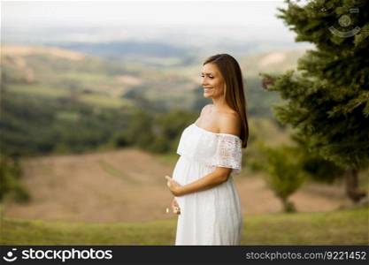 Young pregnant woman in white dress at the summer field