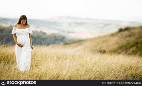 Young pregnant woman in white dress at the summer field