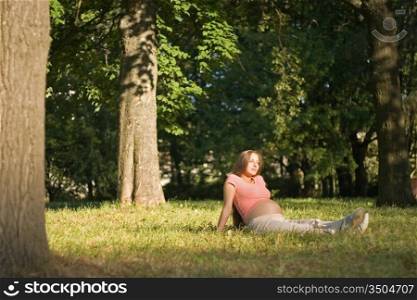 young pregnant woman is sitting in the park among the trees