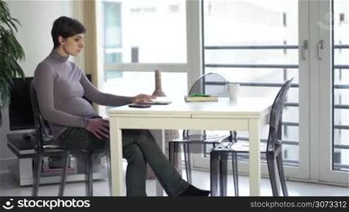 Young pregnant woman relaxing at home with ipad tablet for internet, email, expectant mother sitting in living room with pc computer, talking on cell phone. Happy people recreation, leisure, lifestyle