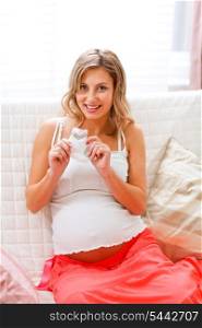 Young pregnant woman sitting on couch with baby&rsquo;s socks in hand&#xA;