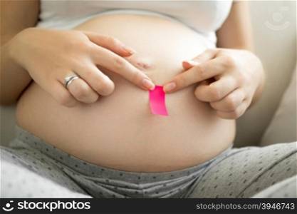 Young pregnant woman sticking pink memo sticker on belly