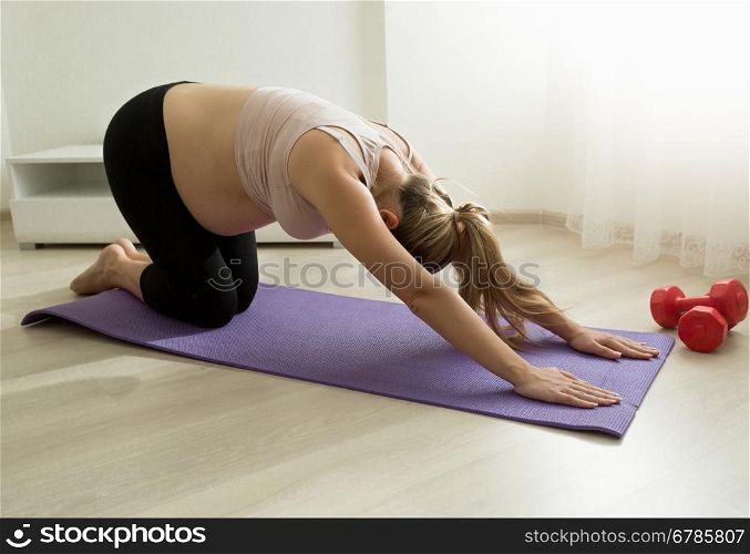Young pregnant woman stretching on fitness rug at home