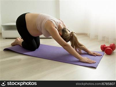 Young pregnant woman stretching on fitness rug at home