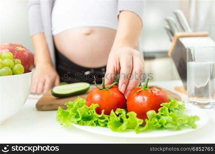 Young pregnant woman taking fresh tomato from plate