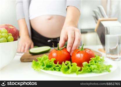 Young pregnant woman taking fresh tomato from plate