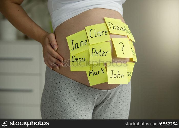 Young pregnant woman with child names on memo stickers on belly