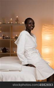 Young pretty african woman sitting at beauty spa salon wearing bathrobe