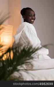 Young pretty african woman sitting at beauty spa salon wearing bathrobe