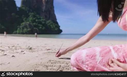 young pretty asian woman sit down use wood stick writing words on the sand beach, playing sand on summer holiday vacation beach, sit down on tropical beach island, travel booking reservation package