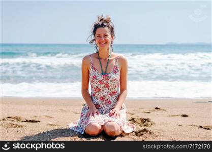 Young pretty beautiful woman sitting on the beach in summer dress smiling happy relaxed smile joy