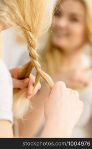 Young pretty blonde woman creating her hairstyle, making braid. Lovely female getting ready. Woman making braid on blonde hair