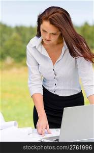 Young pretty businesswoman in sunny nature with laptop behind table