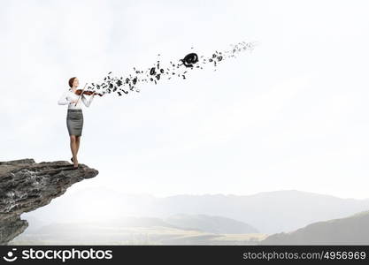 Young pretty businesswoman on rock edge playing violin. My business melody