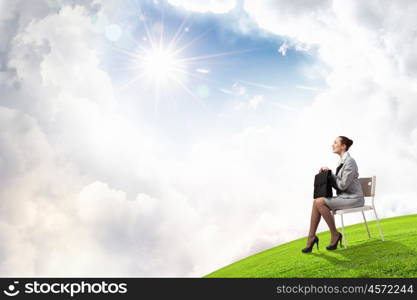 Young pretty businesswoman sitting on chair with briefcase in hands. Taking break from office